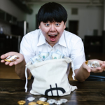 Asian man excitedly holding cryptocurrency and US dollars, symbolizing financial success and wealth.
